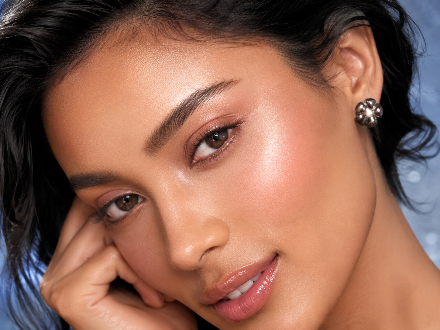 Close-up beauty portrait of a woman with luminous skin, resting her hand against her face