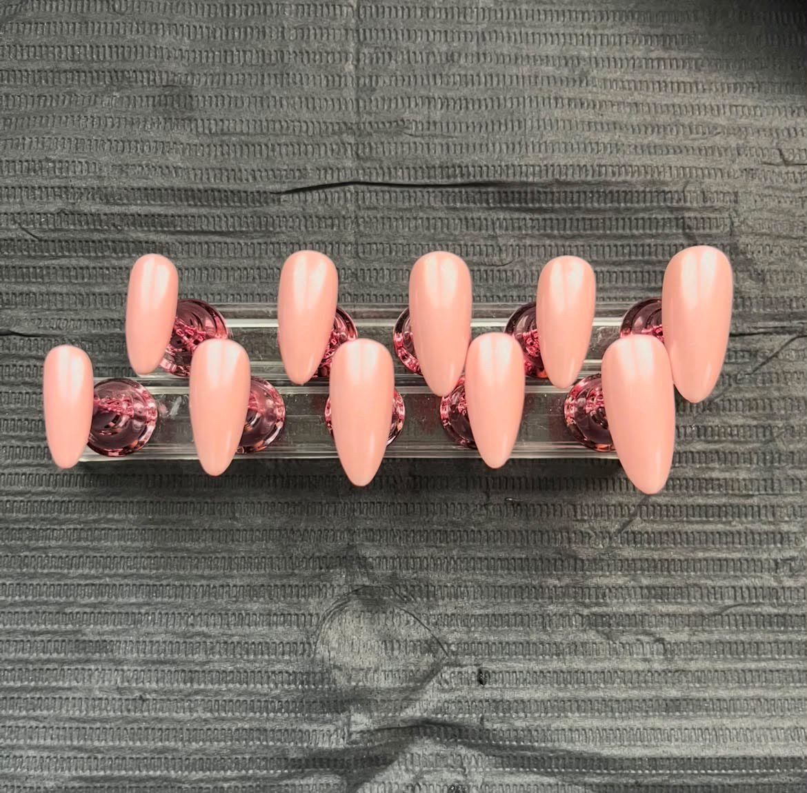 Glossy blush almond nails on a crystal display stand